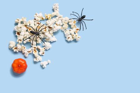 Composition with tasty popcorn, pumpkin and spiders on Halloween celebration on blue backgroundの写真素材