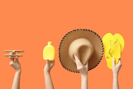Female hands holding summer accessories on orange backgroundの写真素材