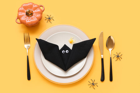 Festive table setting with Halloween bat, pumpkin and spiders on yellow backgroundの写真素材