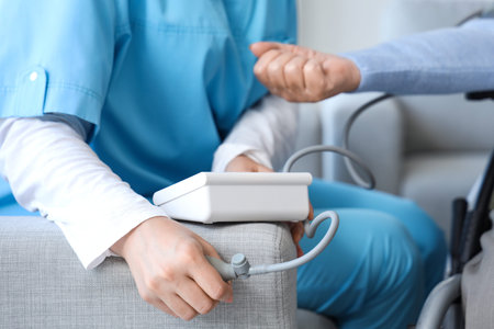 Female nurse measuring blood pressure of senior woman in wheelchair at home, closeup