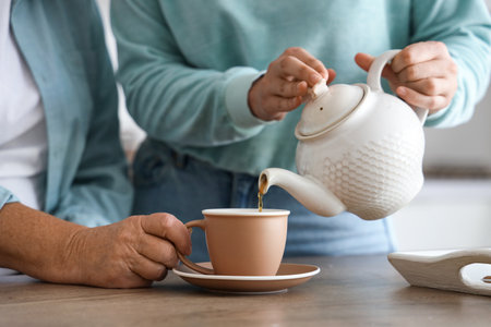 Young woman pouring hot tea for her mother in kitchen, closeupの写真素材