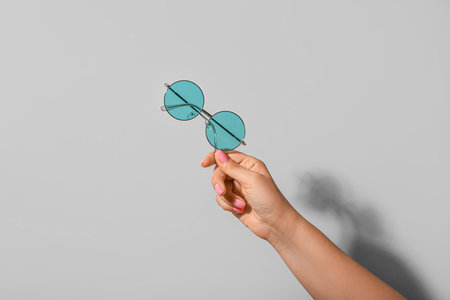 Woman holding stylish sunglasses on gray background