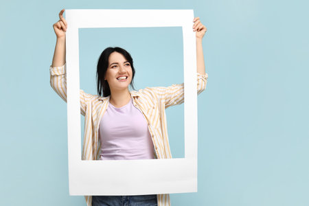 Portrait of happy young brunette with frame on blue backgroundの写真素材