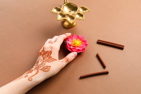 Female hand with diya lamp, cinnamon and lotus flower for celebration of Divaly on brown background