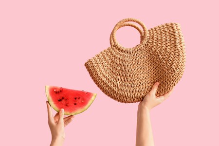 Female hands with slice of fresh watermelon and wicker bag on pink backgroundの写真素材