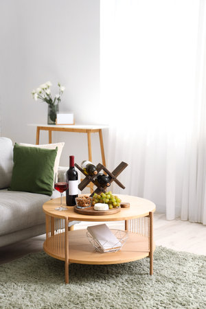 Stylish living room interior with stand of wine bottles and snacks on tableの写真素材