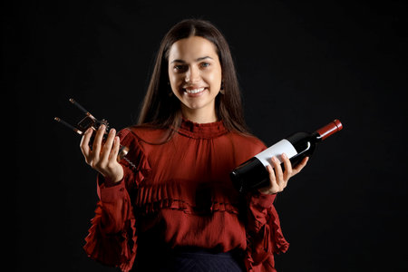Young woman with glass and bottle of wine on black backgroundの写真素材