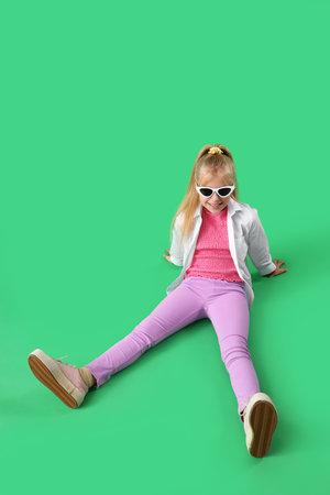 Stylish little girl sitting on green backgroundの写真素材