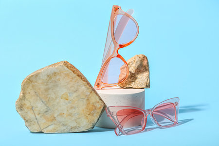 Decorative podium and stones with stylish sunglasses on blue backgroundの写真素材