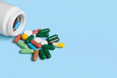 Jar with different scattered pills on blue background