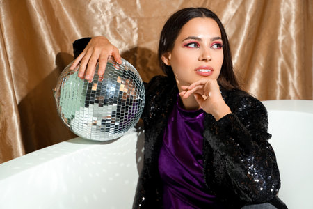 Stylish young woman with disco ball in bathtubの写真素材