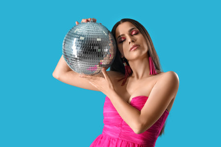 Stylish young woman with disco ball on blue backgroundの写真素材