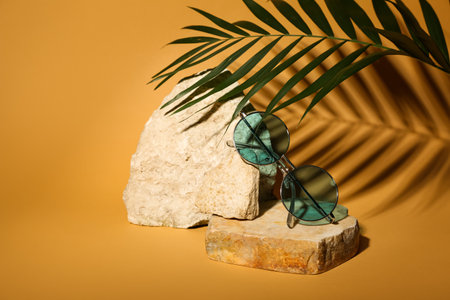 Stones with stylish modern sunglasses and palm leaf on orange backgroundの写真素材