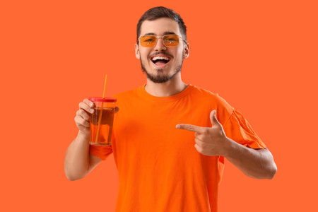 Young man pointing at glass of juice on red backgroundの写真素材