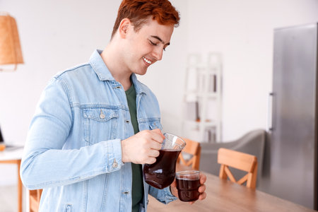 Young man pouring juice into glass in kitchenの写真素材