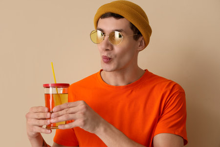 Young man with glass of juice blowing kiss on beige background, closeupの写真素材