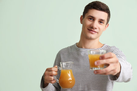 Young man with jug and glass of juice on green backgroundの写真素材