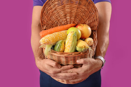 Mature male farmer with wicker basket full of ripe vegetables on purple backgroundの写真素材