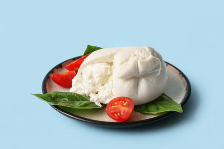 Plate of tasty Burrata cheese with basil and tomatoes on blue backgroundの写真素材