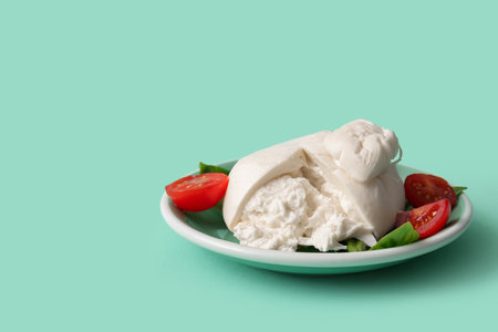Plate of tasty Burrata cheese with basil and tomatoes on turquoise backgroundの写真素材