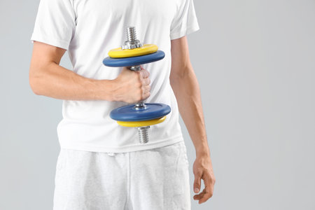Young man with dumbbell on gray backgroundの写真素材