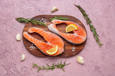 Wooden board with raw salmon steaks and different spices on pink backgroundの写真素材