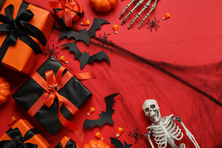 Composition with gift boxes, tasty candy corns, skeleton and Halloween decor on red backgroundの写真素材