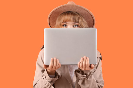Stylish young woman in fall clothes with laptop on orange backgroundの写真素材