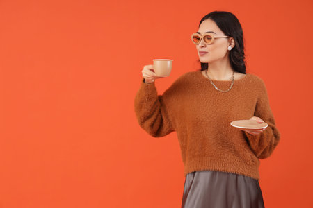 Stylish young Asian woman in fall clothes with coffee cup on red backgroundの写真素材