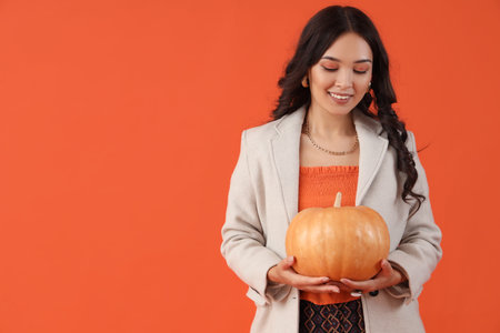 Stylish young Asian woman in fall clothes with pumpkin on red backgroundの写真素材