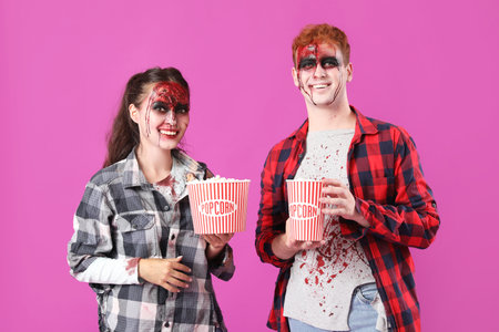 Young couple dressed for Halloween with popcorn on pink backgroundの写真素材