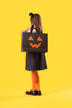 Little girl dressed for Halloween with gift bag on yellow backgroundの写真素材