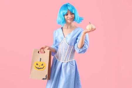 Young woman dressed for Halloween with gift bag and pumpkin on pink backgroundの写真素材