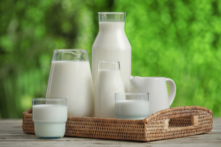 Glasses and bottles of fresh milk on white wooden table outdoorsの写真素材
