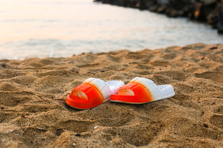 Stylish flips flops on sand near ocean at resort