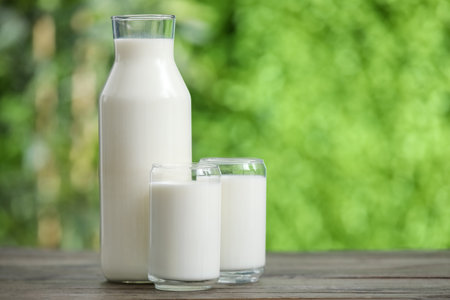 Glasses and bottle of fresh milk on wooden table outdoorsの写真素材