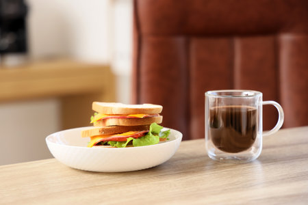Plate with tasty sandwiches and cup of coffee on wooden table in office, closeupの写真素材