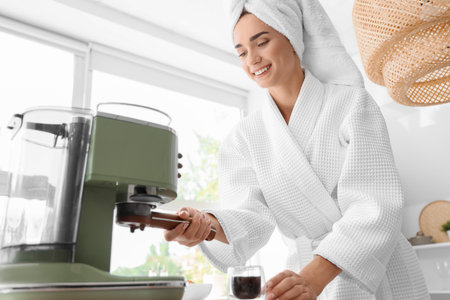 Beautiful young woman in bathrobe using coffee machine at kitchenの写真素材