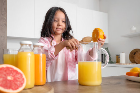 Little Asian girl making fresh citrus juice at table in kitchenの写真素材