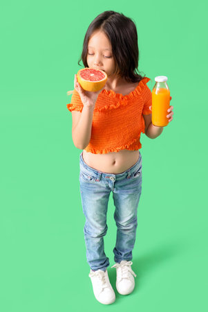 Little Asian girl with bottle of fresh citrus juice and grapefruit slice on green backgroundの写真素材