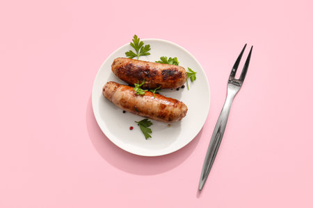 Plate of tasty grilled sausages and fork on pink backgroundの写真素材