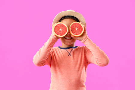 Little African-American boy with slices of fresh grapefruit on purple backgroundの写真素材