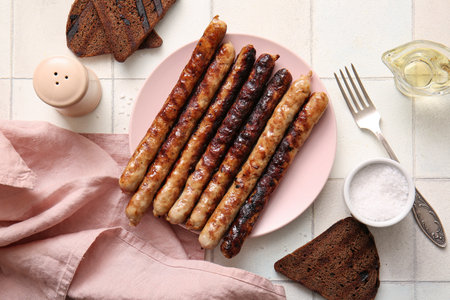 Plate of tasty grilled sausages on white tile backgroundの写真素材