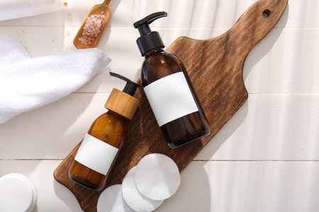 Bottles of shampoo, sea salt and cotton pads on white wooden backgroundの写真素材