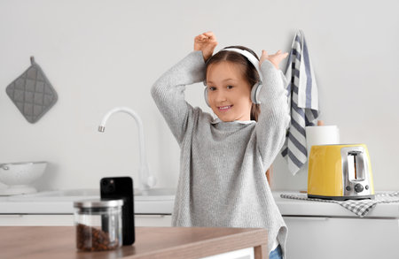 Little girl with headphones listening to music and dancing in kitchen at homeの写真素材