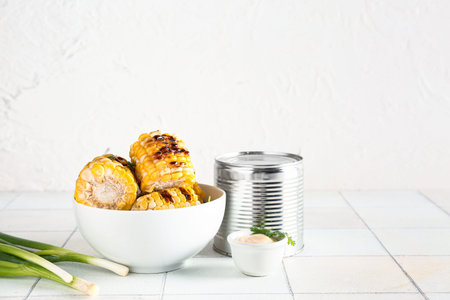 Bowl with tasty grilled corn cobs and green onion on white tile table