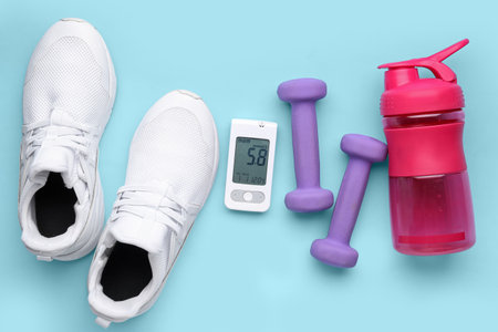 Glucometer with bottle of water, dumbbells and sneakers on blue background. Diabetes conceptの写真素材