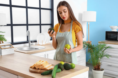 Young woman with avocado and apple in kitchen