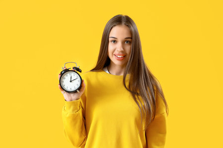 Young woman with alarm clock on yellow background