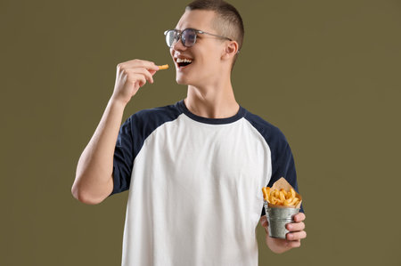 Young man eating French fries on color backgroundの写真素材